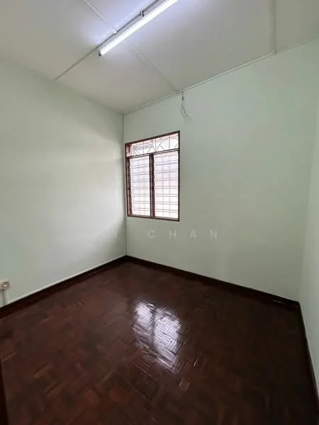 Room features: light green painted walls, wooden parquet flooring, single window with metal grille, ceiling light fixture, no visible furniture, empty room.
