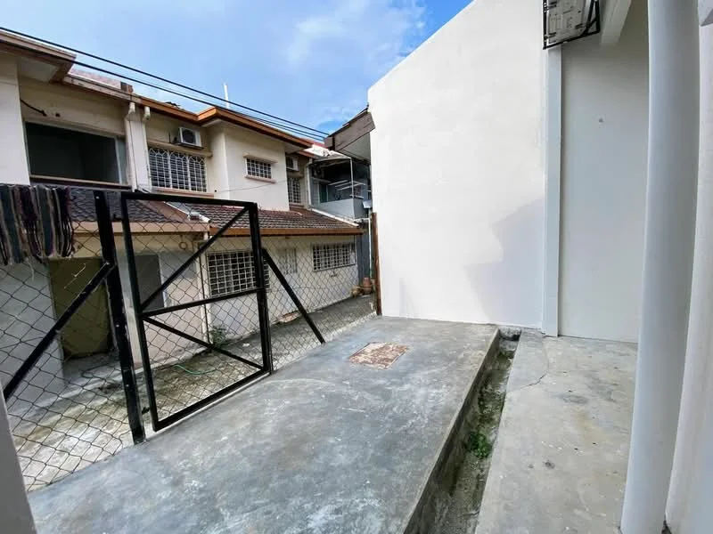 Exterior features: concrete flooring, fenced area, white painted walls, access gate, surrounding buildings, clear sky.