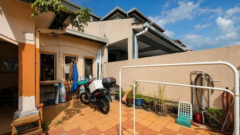 Exterior type: linked terrace house; features: paved patio, motorbike parked, outdoor clothes drying rack, planters with greenery, exterior wall with light color, roof overhang, windows with wooden frames, blue sky with clouds; style: modern.