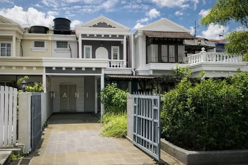 Exterior type: linked terrace house; features: white painted facade, gabled roof, balcony with railing, two water tanks on roof, manicured garden, paved driveway, metal gate, front porch, window with wooden frame, decorative columns, surrounded by greenery; style: modern.