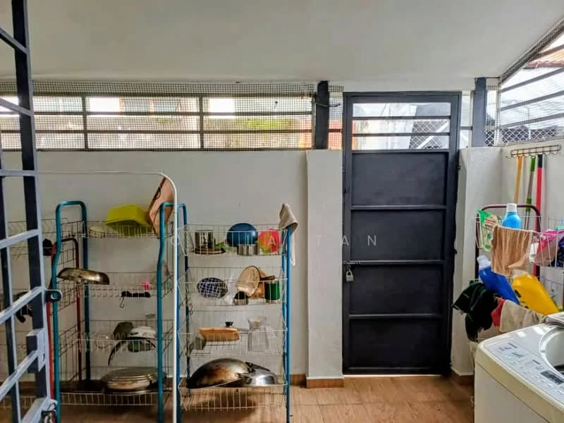 Laundry features: metal shelving unit with dishes, white walls, wood-look vinyl flooring, black metal door, window with metal grille, washing machine, various cleaning supplies, broom and mop, hanging drying rack.