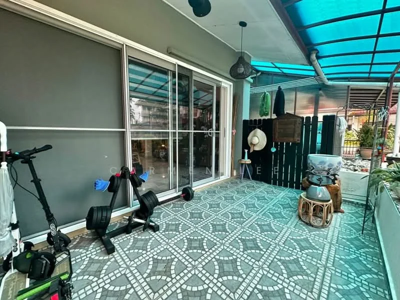 Room features: sliding glass door, grey walls, decorative wall paneling, outdoor flooring with patterned tiles, hanging pendant light, exercise equipment, decorative stool, potted plants, outdoor furniture, green awning; style: modern; view: garden.
