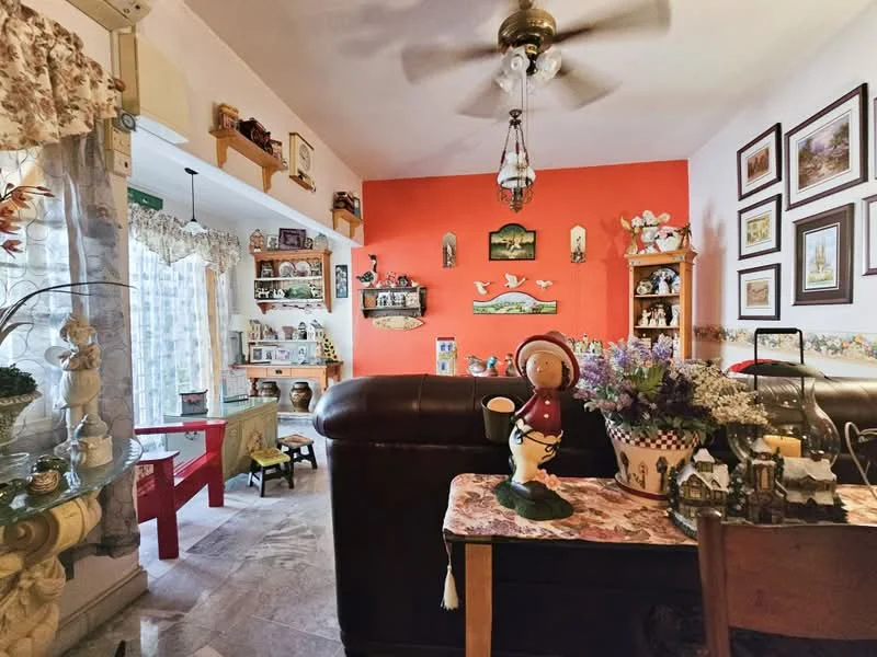 Living features: brown leather sofa, decorative throw pillows, wooden coffee table, ceiling fan with light, wall-mounted decorative shelves, various decorative items on shelves, orange accent wall, framed artwork on walls, table lamp, curtains with floral pattern, marble flooring, decorative tablecloth; style: traditional.