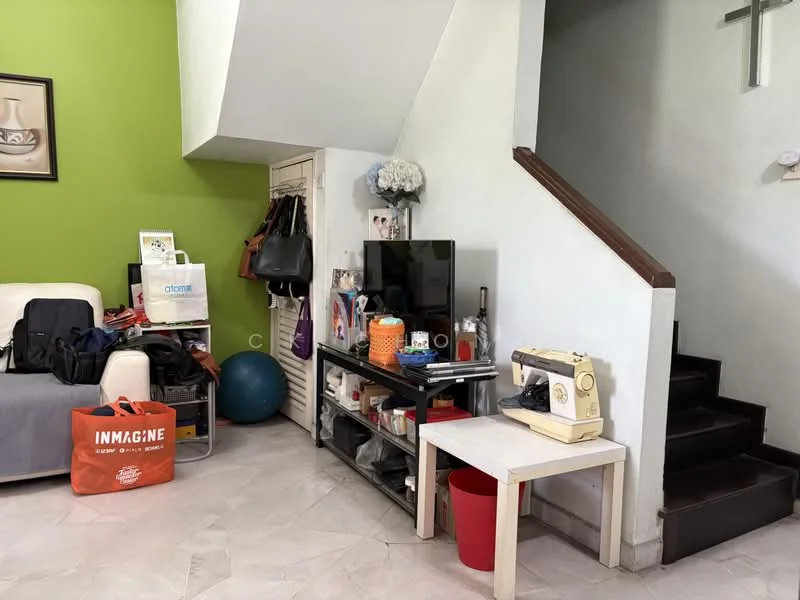 Living features: green accent wall, white painted walls, marble tile flooring, sofa in cream color, TV on a black console, sewing machine on a white table, decorative flower arrangement, storage cabinet, exercise ball, staircase leading to upper floor, various bags and items on the floor; style: modern.