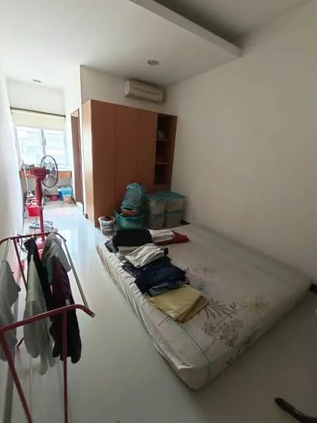 Bedroom features: single bed with floral bedding, built-in wardrobe with wooden doors, white painted walls, glossy tile flooring, window with sheer curtains, ceiling-mounted air conditioning unit, clothes drying rack, laundry basket, folded clothes on bed.