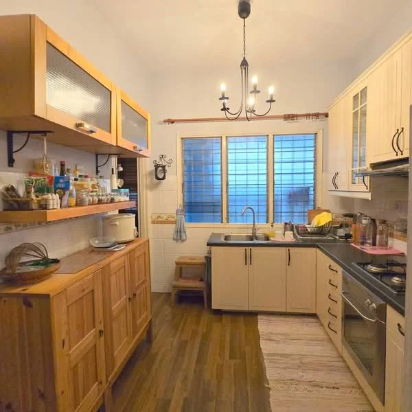 Kitchen features: wooden cabinetry with glass fronts, cream painted walls, dark countertop, stainless-steel sink, chrome pull-down faucet, built-in oven, freestanding gas range oven, wooden dining table, wooden flooring, chandelier light fixture, window with grid pattern, open shelving, decorative wall sconce; style: modern.