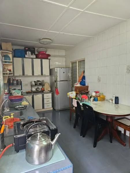 Kitchen features: stainless-steel fridge, built-in cabinets with cream finish, white tiled walls, grey tiled flooring, gas stove with 4 burners, kettle on stove, round dining table, black plastic dining chairs, sink with faucet, window with blinds, various kitchen utensils and containers on counter; style: functional.