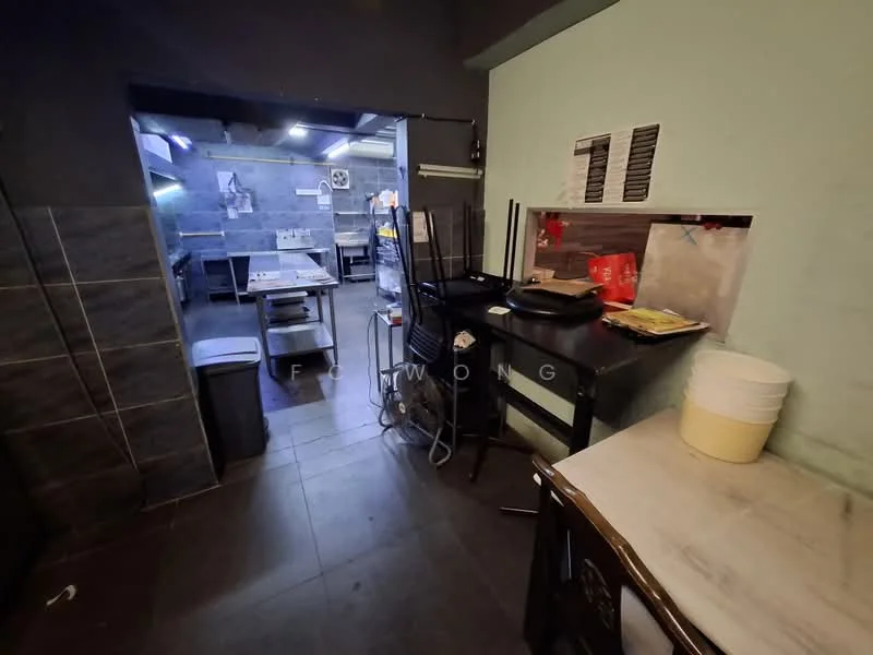 Kitchen features: grey tiled walls, black countertop, stainless-steel work table, metal shelving unit, industrial sink, tile flooring, overhead lighting, kitchen equipment visible, waste bin, open layout; style: industrial.