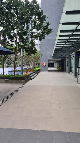 Exterior type: landscape garden; features: paved walkway, manicured landscaping, tropical trees, sitting area with shade, safety buoy, modern building facade, outdoor lighting, water feature, pool area in background; style: modern.