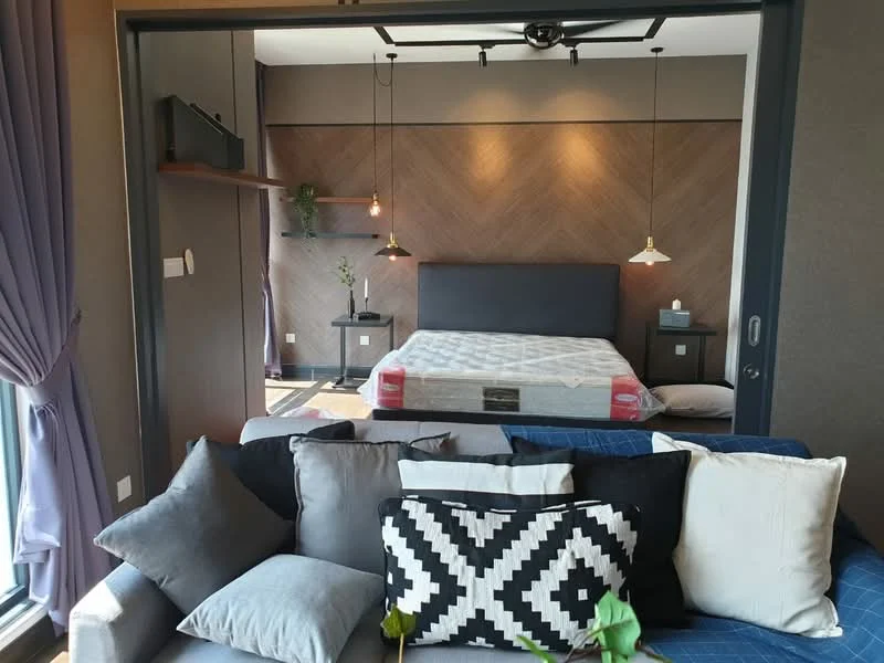 Living features: sofa with multiple cushions, decorative black and white patterned cushion, wooden accent wall with herringbone pattern, hanging pendant lights, floor-to-ceiling window with sheer curtains, plant on shelf, open shelving unit, wooden flooring; style: modern; view: city. Bedroom features: queen-size bed with mattress, wooden headboard, nightstand, wall-mounted light fixtures, decorative plant, grey bedding; style: modern.