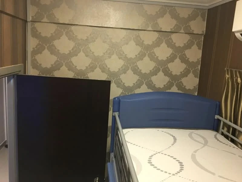 Bedroom features: blue bed frame, mattress with patterned bedding, decorative wallpaper with damask pattern, cream painted walls, wooden door, curtains with striped pattern, air conditioning unit; style: modern.