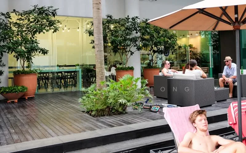 Exterior type: clubhouse; features: wooden deck flooring, large glass windows, outdoor seating area with grey wicker furniture, potted plants, tropical landscaping, sunshade umbrella, manicured greenery, open-air dining area, modern architectural design; style: modern.