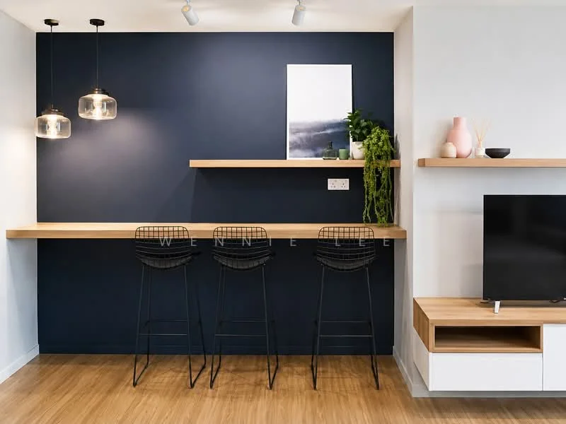 Room features: dark blue accent wall, wooden shelf, black metal bar stools, pendant lighting, light wood flooring, white wall-mounted TV console, decorative plants, framed artwork, decorative vases; style: modern.