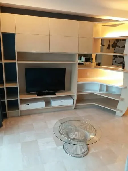 Living features: built-in cabinetry with light wood finish, open shelving, TV console, wall-mounted TV, glass display shelves, marble flooring, round wire coffee table, ambient lighting, mirrored backsplash, decorative wall art; style: modern.