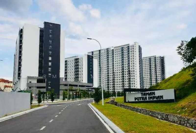 Exterior type: high-rise condominium; features: modern facade with a combination of dark and light colors, multiple storeys visible, landscaped green area in front, asphalt road leading to the entrance, signage for Taman Putra Impian, surrounding greenery, parking area visible, well-maintained exterior, balconies on upper floors; style: modern.