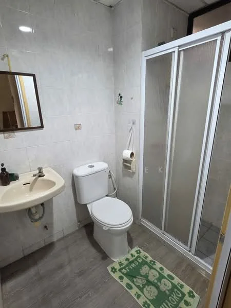 Bathroom features: white tiled walls, grey tiled flooring, single-sink vanity with cream countertop, one-piece toilet, walk-in shower with glass enclosure, framed mirror, toilet paper holder, bath mat with green design.