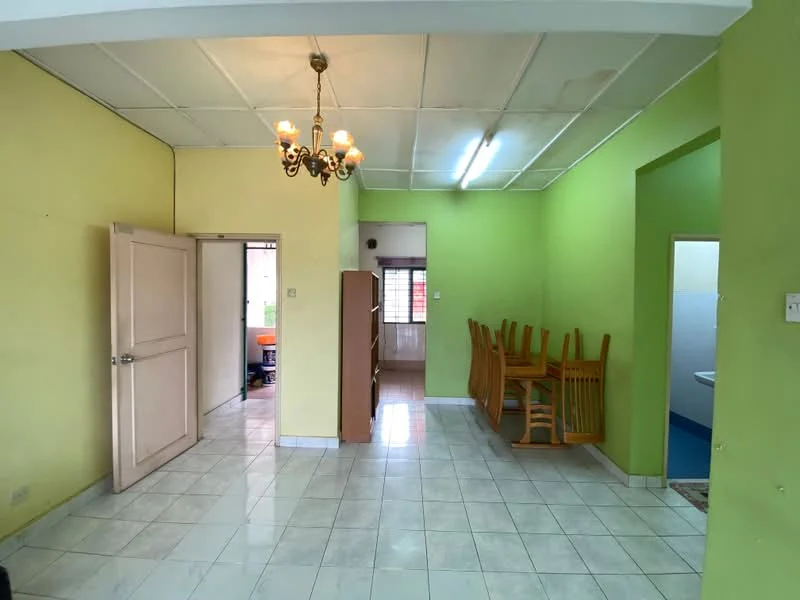 Room features: green painted walls, white tiled flooring, ceiling with exposed beams, chandelier light fixture, doorway leading to another room, wooden dining chairs stacked, window with natural light, open layout, corner with bathroom door.