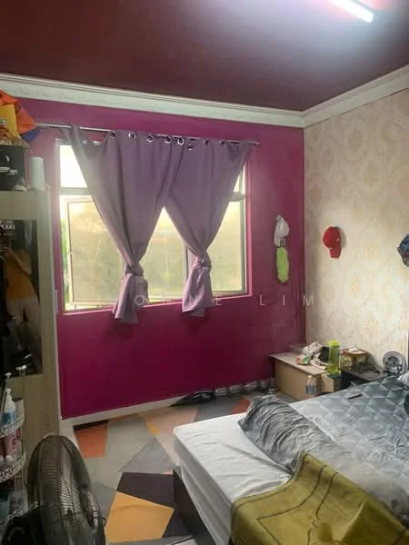 Bedroom features: pink painted walls, cream patterned wallpaper, window with sheer curtains, single bed with grey bedding, area rug with geometric pattern, ceiling fan, wooden bedside table, clothes hanging on wall, decorative hats on wall, fan on floor.