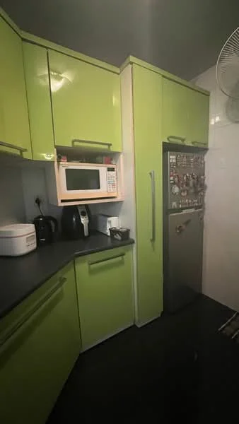 Kitchen features: green high-gloss cabinetry, black countertop, built-in microwave, stainless-steel fridge, kettle, coffee machine, black appliances, wall-mounted fan, tile backsplash; style: modern.