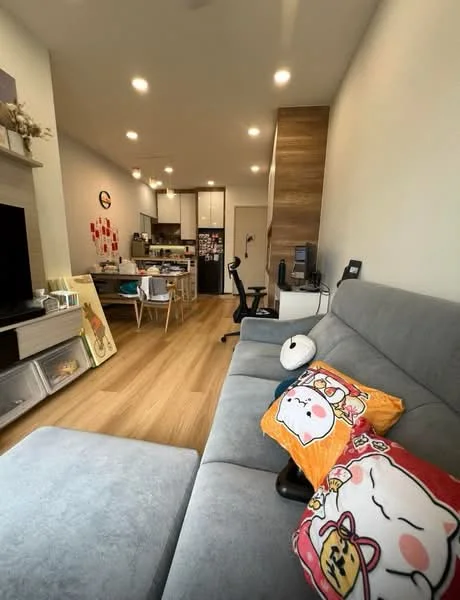 Living features: grey fabric sofa, decorative cushions with cartoon characters, wooden flooring, wall-mounted TV, TV console, recessed LED downlights, open-plan layout to kitchen, study desk with chair, wall-mounted shelves, decorative wall art, air conditioning unit; style: modern. Kitchen features: white cabinetry, stainless-steel appliances, kitchen island, open shelving, refrigerator, microwave, countertop, tile backsplash; style: modern.