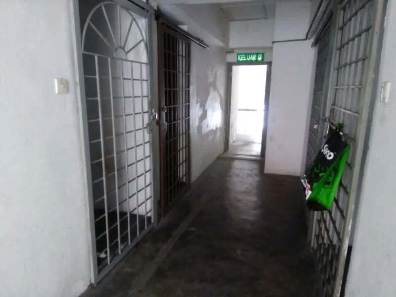 Room features: concrete flooring, white painted walls, metal security grilles on doors, exit sign, dim lighting, narrow corridor, door frames, visible exit at the end of the corridor.
