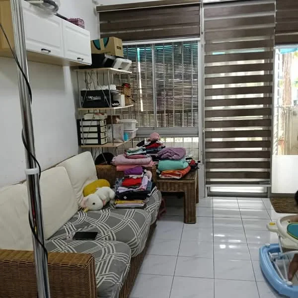 Living features: sofa with patterned upholstery, coffee table, white walls, tile flooring, roller blinds, built-in shelving unit, decorative items on shelves, stacked laundry on sofa, floor-to-ceiling windows, light from windows.