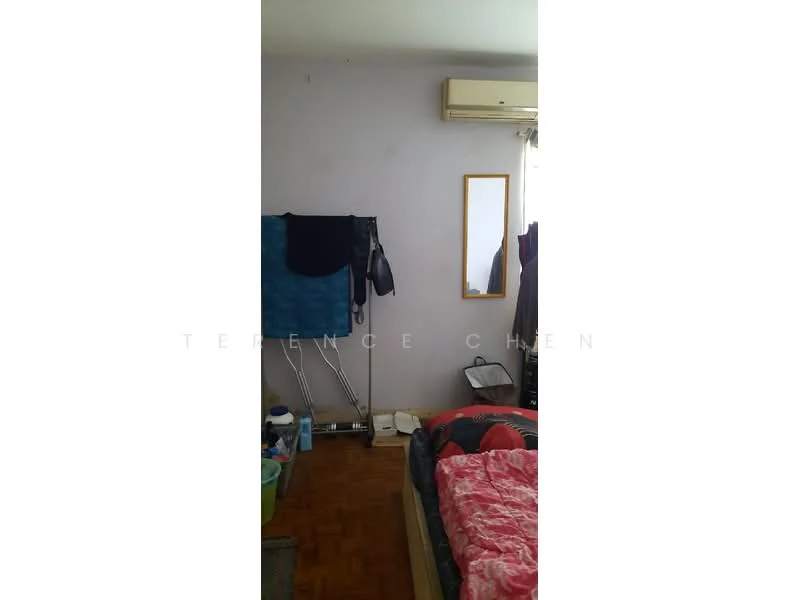 Bedroom features: wooden flooring, light purple painted walls, window with sheer curtains, mirror on wall, air conditioning unit, bed with red and black bedding, clothes rack, various storage containers, decorative items on floor.