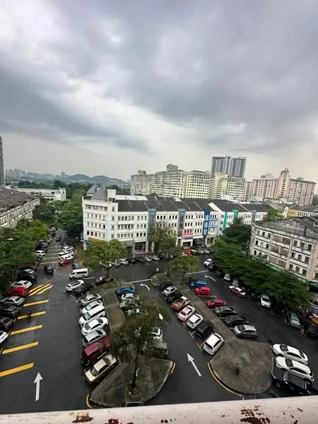 Exterior type: low-rise apartment block; features: multi-storey buildings, mixed facade colours, parking lot with marked spaces, surrounding greenery, urban context with city skyline, cloudy sky; style: modern.