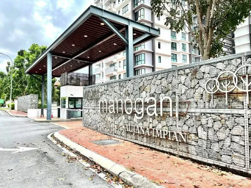 Exterior type: gated community; features: stone-clad entrance wall, modern guardhouse, landscaped greenery, paved driveway, signage with name 'Manogan', overhead canopy, surrounding trees, curved road leading to entrance; style: modern.