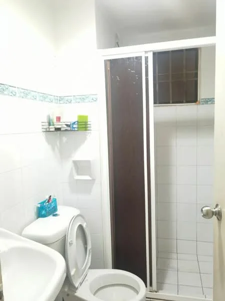 Bathroom features: white tiled walls, white tiled flooring, one-piece toilet, shower with glass door, chrome shower head, shelf for toiletries, toilet paper holder, small storage basket, decorative border tile, mirror above sink.