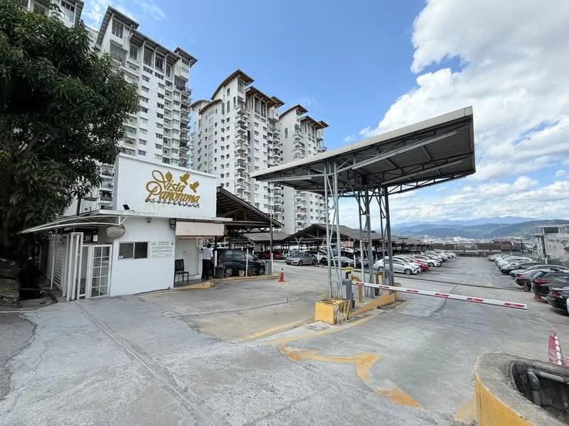 Exterior type: high-rise condominium; features: multi-storey car park, covered parking, guard house at entrance, gated entry, landscaped area with trees, signage with 'Vista Panorama', concrete facade, surrounded by mountain view; style: modern.