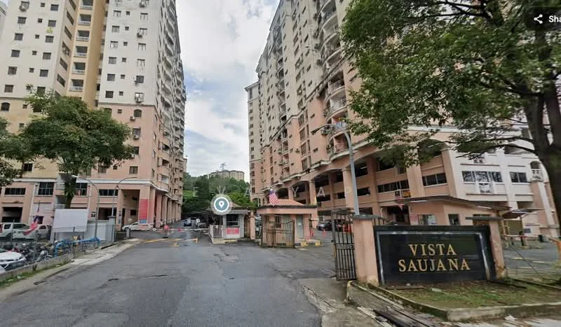 Exterior type: high-rise condominium; features: pink painted facade, guard house at entrance, gated entry, surrounded by mature greenery, driveway with interlocking pavers, multiple storeys, main entrance sign, parking area visible; style: modern.