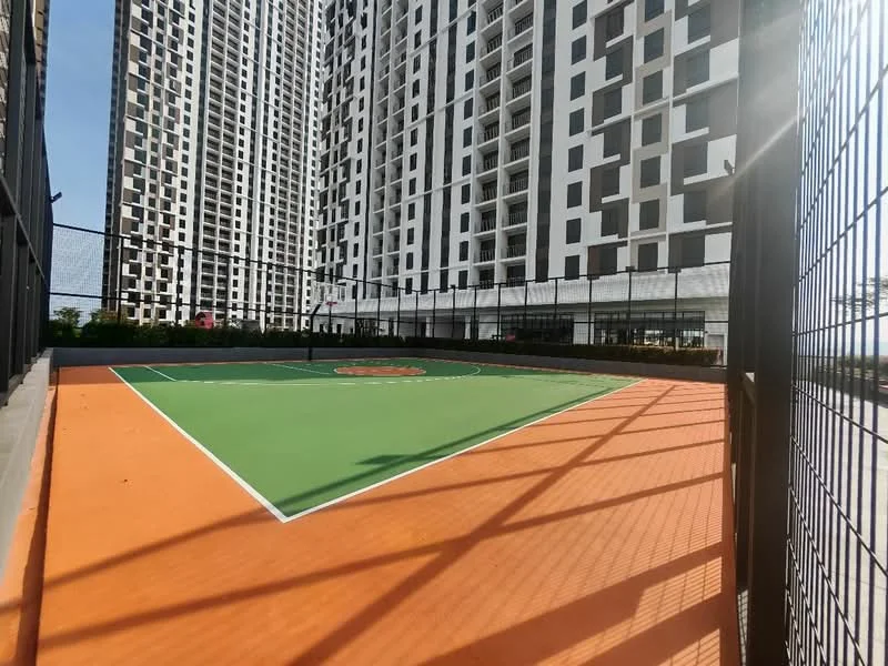 Exterior type: high-rise condominium; features: basketball court, green playing surface, orange boundary lines, surrounded by fencing, high-rise buildings in background, landscaped area around court; style: modern.