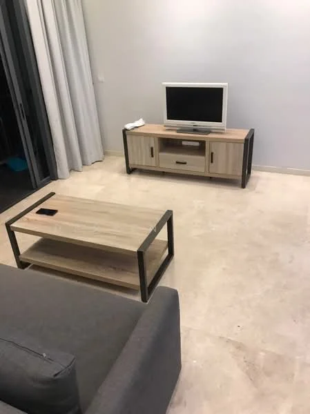 Living features: grey fabric sofa, wooden coffee table with metal legs, wooden TV console with drawers, flat-screen TV, light-colored stone flooring, white walls, floor-to-ceiling curtains, open layout; style: modern.