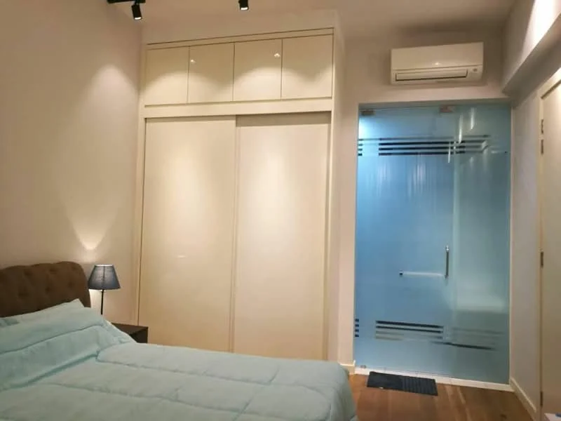 Bedroom features: queen-size bed with upholstered headboard, light blue bedding, built-in wardrobe with sliding doors, wooden flooring, wall-mounted air conditioning unit, table lamp on bedside table, glass shower enclosure, recessed ceiling lights; style: modern.