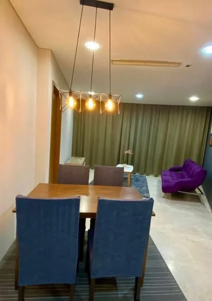 Dining features: wooden dining table, 4 upholstered dining chairs in blue, pendant light fixture with 5 bulbs, cream painted walls, marble tile flooring, floor-to-ceiling curtains in brown, area rug with striped pattern, purple fabric sofa, wall-mounted decor, recessed ceiling lights; style: modern.