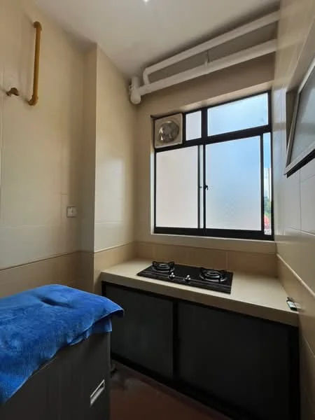 Kitchen features: light beige tiled walls, light beige tiled flooring, window with grid pattern, two-burner gas hob, countertop with light beige surface, exhaust fan, golden pipe, grey cabinet under countertop; style: modern.