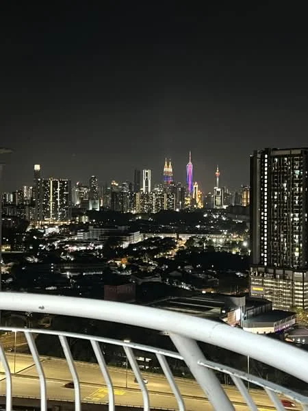 Exterior type: high-rise condominium; features: city skyline view, night lighting, balcony railing, surrounding urban landscape, visible high-rise buildings, illuminated landmarks, street view below; style: modern.