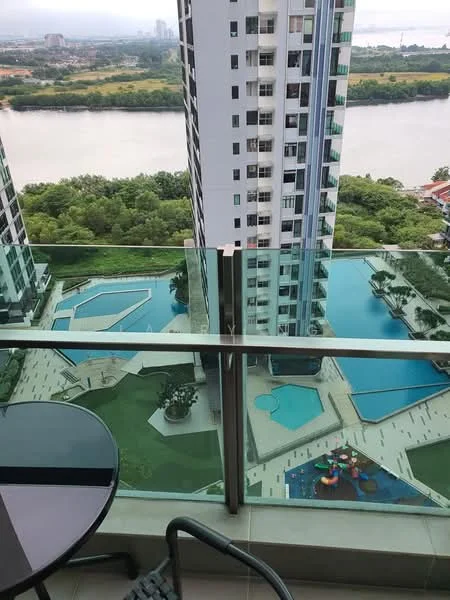 Room features: balcony with glass railing, outdoor seating area with round table and chairs, view of swimming pools, view of landscaped gardens, view of river, high-rise building structure, concrete flooring, greenery in the vicinity; style: modern; view: river.