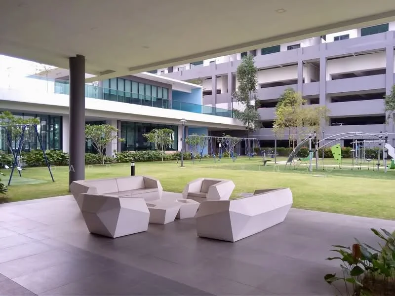 Exterior type: clubhouse; features: outdoor seating area with modern geometric furniture, manicured lawn, landscaped garden with trees, children's playground, walking path, surrounding greenery, multi-storey car park in background, glass facade of clubhouse, lighting fixtures along path; style: modern.