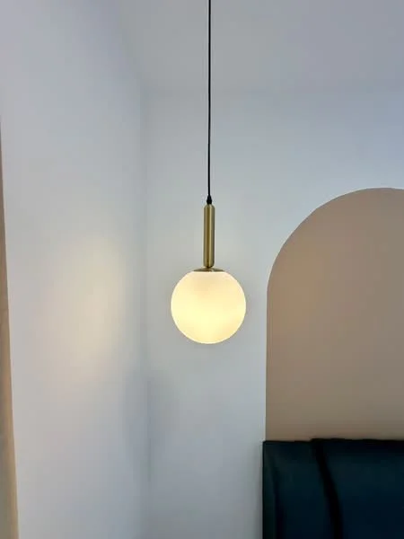 Room features: pendant light with round glass shade, brass finish, white walls, arched wall feature; style: modern.