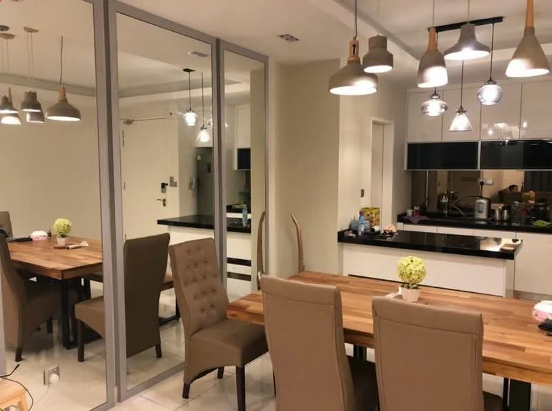 Dining features: wooden dining table, 6 upholstered dining chairs in beige, pendant lighting with multiple bulbs, mirrored wall, black countertop, white cabinetry, kitchen appliances visible in background, neutral wall color, tile flooring; style: modern.