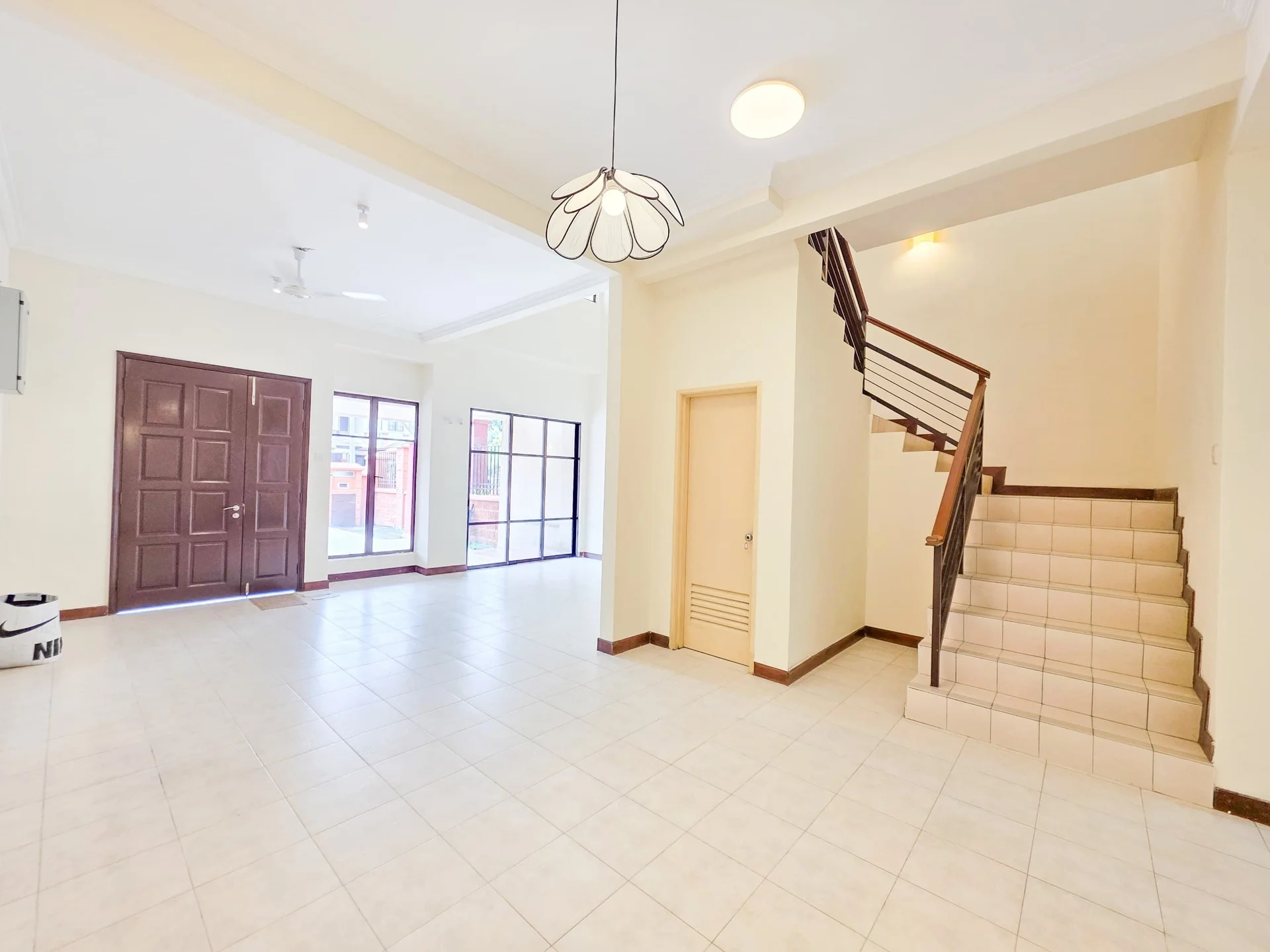 Living features: cream painted walls, tile flooring, 5-blade ceiling fan, large windows, double main door, staircase with wooden railing, recessed ceiling lights, natural light from windows; style: modern. Room features: cream painted walls, tile flooring, staircase with wooden railing, doorway leading to unknown area.