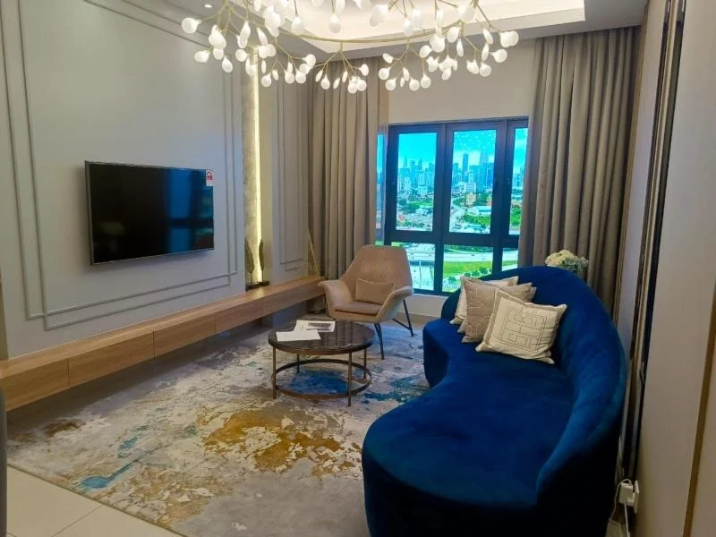 Living features: blue curved sofa, round coffee table, wall-mounted TV, wooden TV console, area rug with abstract pattern, floor-to-ceiling windows, curtains, chandelier with multiple bulbs, decorative plant, wall paneling with decorative moulding; style: modern; view: city.