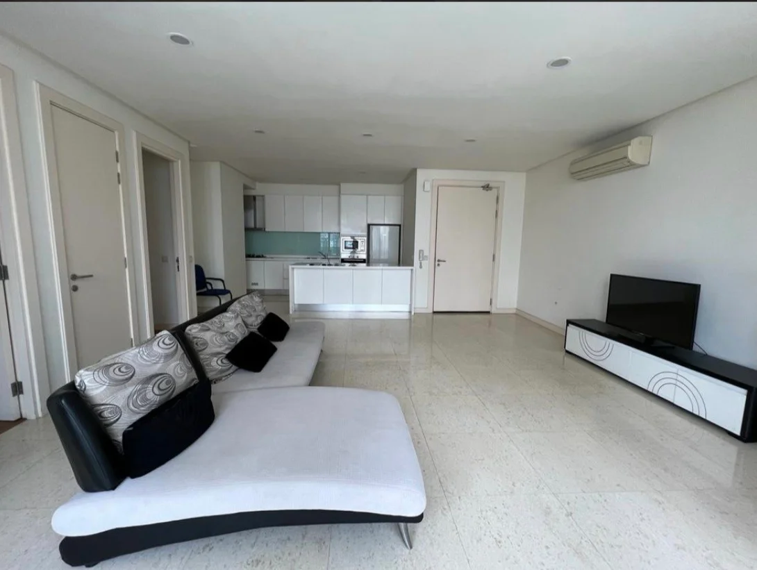 Living features: 3-seater fabric sofa in white with black accents, coffee table with geometric design, wall-mounted TV, TV console with storage, marble flooring, recessed downlights, air conditioning unit, open layout to kitchen, neutral painted walls, floor-to-ceiling windows, sliding door to balcony, decorative cushions; style: modern. Kitchen features: white cabinetry, stainless-steel built-in oven, microwave, ceramic cooktop, kitchen island, white countertops, refrigerator, open shelving; style: modern.