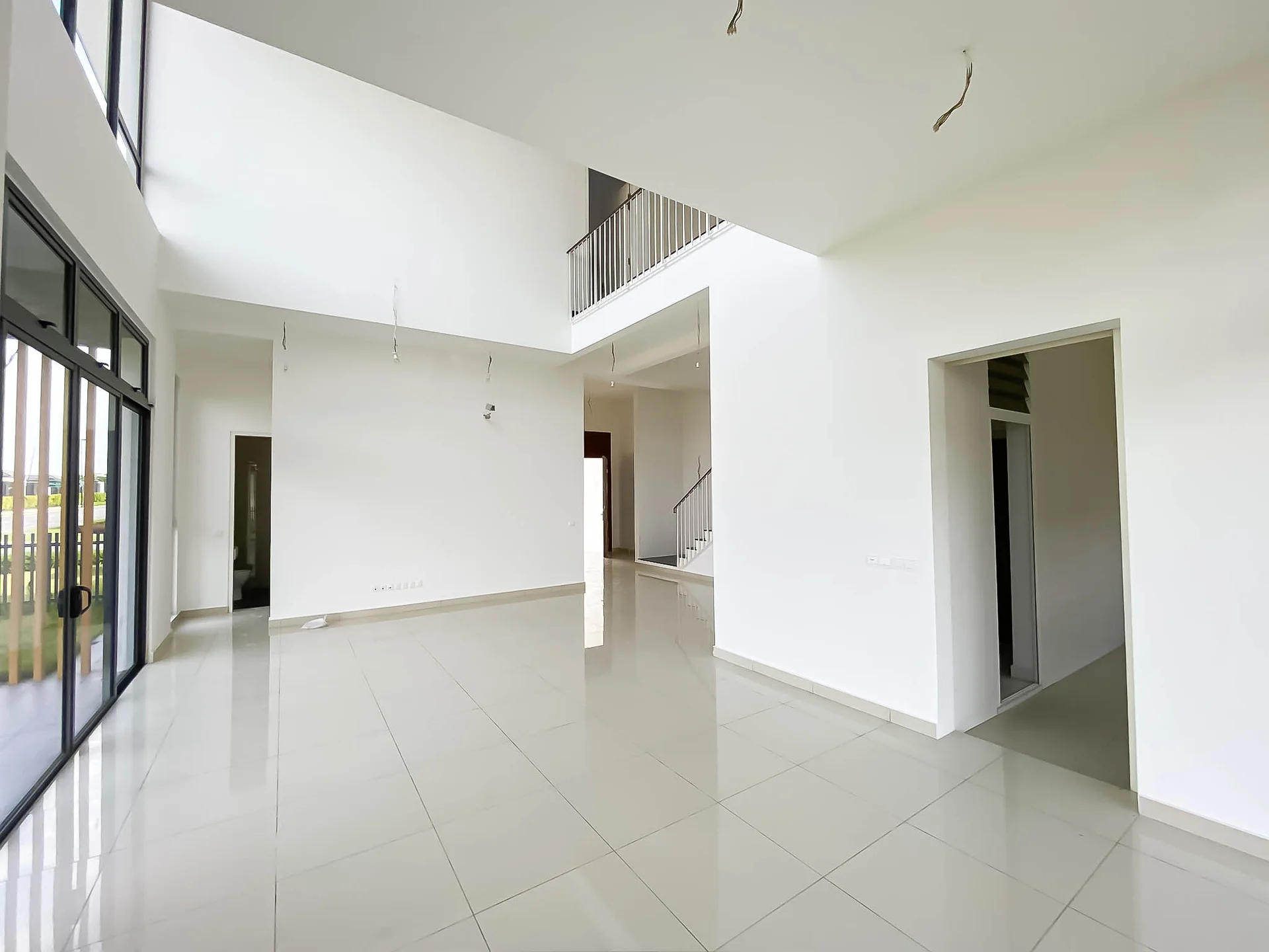 Living features: white painted walls, grey tiled flooring, double-height ceiling, floor-to-ceiling windows, sliding glass door, open layout, staircase with railing, natural light from windows; style: modern; view: garden. Room features: white painted walls, grey tiled flooring, doorway leading to another room.