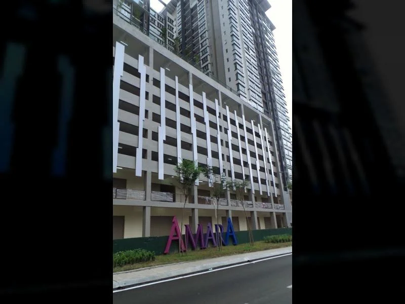 Exterior type: mid-rise condominium; features: multi-storey car park, glass curtain wall, white painted facade, projecting balconies, landscaped area with trees, prominent signage, surrounded by road; style: modern.