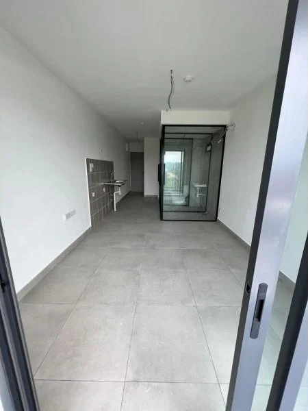 Room features: grey tiled flooring, white painted walls, glass partition, open layout, kitchenette area with wall cabinets, large windows for natural light, ceiling with exposed wiring, no visible furniture; style: modern; view: city.