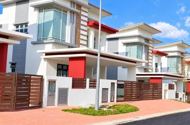 Exterior type: linked terrace house; features: double-storey, white painted facade, grey accent panels, red accent cladding, projecting balconies, flat roof, large corner windows, glass balcony railings, brown horizontal-slat fence, gated entry, driveway with interlocking pavers, fronts a quiet residential street, small landscaped verge; style: modern.