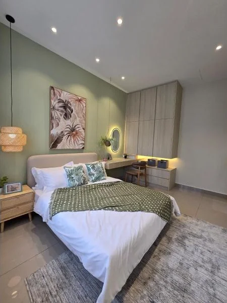 Bedroom features: queen-size bed with white bedding, green throw blanket, decorative pillows with floral pattern, wooden bedside table, framed artwork with tropical theme, green accent wall, built-in wardrobe with light wood finish, study desk with integrated lighting, wall-mounted mirror, recessed downlights, area rug with neutral tones, large window with natural light; style: modern.